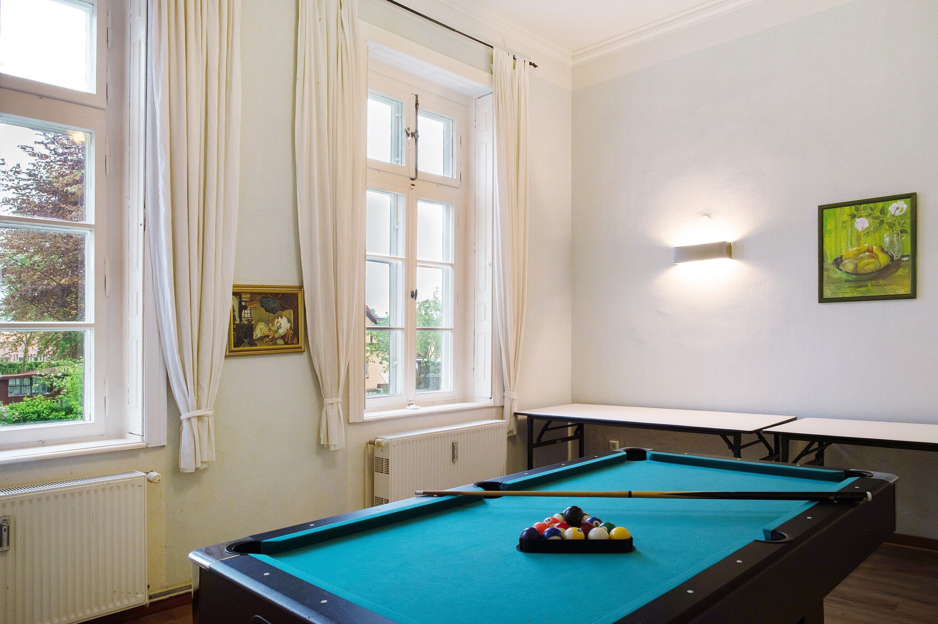Une table de billard dans une pièce avec une fenêtre, un radiateur et un tableau accroché au mur.