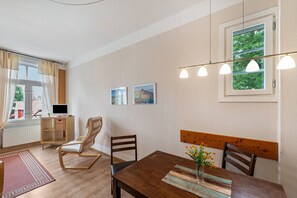 Un coin repas comprenant une table en bois, des chaises, un banc, un petit meuble et une fenêtre avec des rideaux.