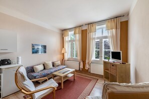Une pièce comprenant un lit, un canapé, une petite table, un téléviseur, une lampe et une fenêtre avec des rideaux.