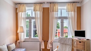 A room with a sofa, a chair, a TV on a wooden stand, and a window with curtains. - Apartment 'Ferienwohnung 9' with Shared Terrace and Shared Garden (Krakow am See)