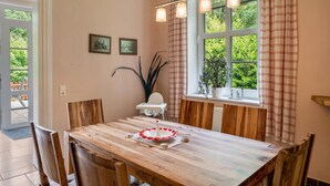 Un coin repas comprenant une table en bois, des chaises, une petite table blanche et une fenêtre avec des rideaux.