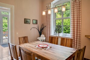 A dining area with a wooden table, chairs, a small white table, and a window with curtains. - Apartment 'Ferienwohnung 10 - Barrierefrei' with Private Terrace and Shared Garden (Krakow am See)
