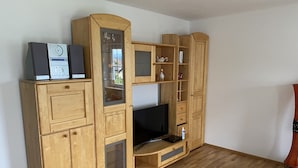 Een houten tv-meubel met een flatscreen televisie, ingebouwde speakers en een vitrinekast met glazen deurtjes.