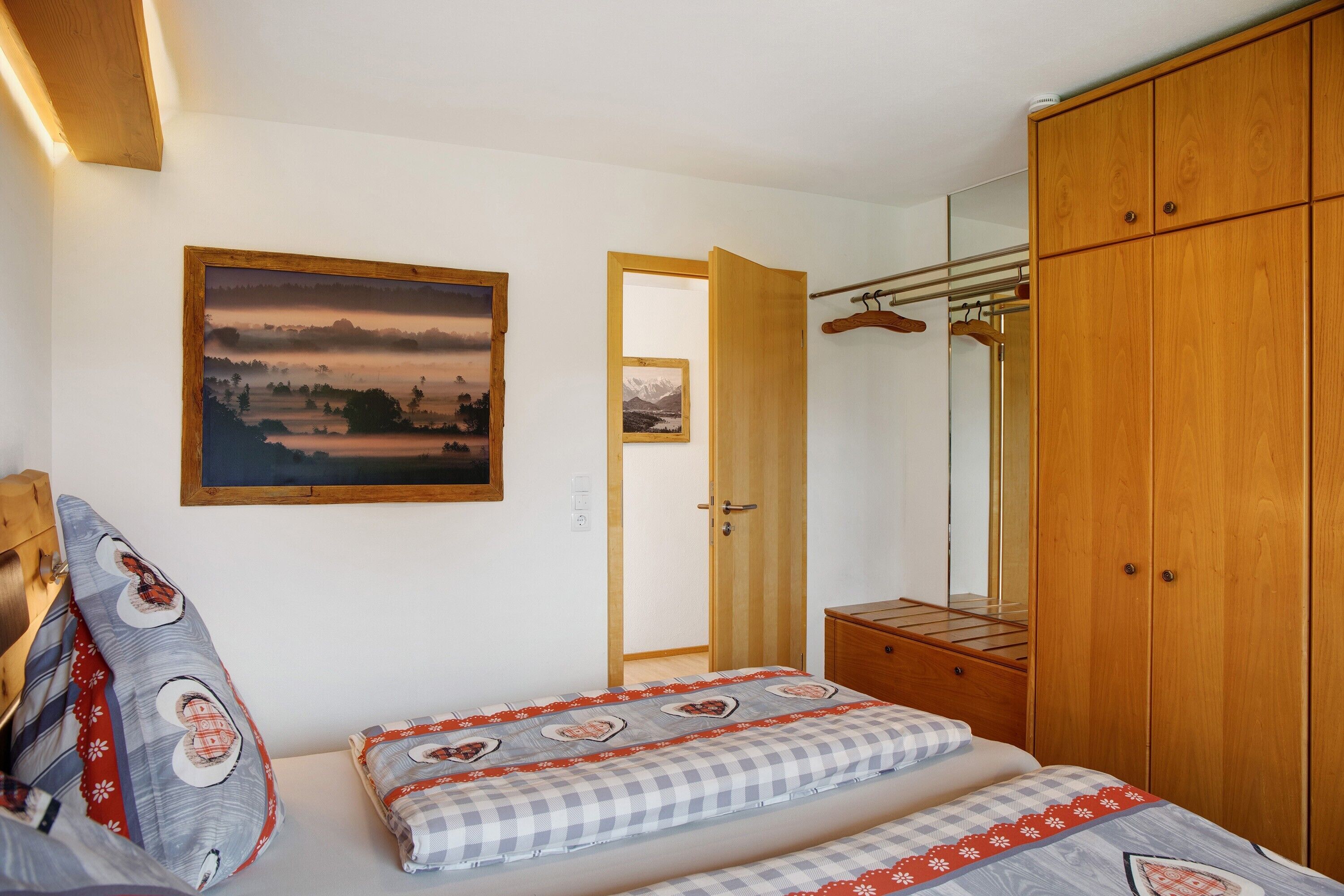 Ein Schlafzimmer mit einem Bett, einem Holzschrank, einem Schminkspiegel und einer Tür zu einem anderen Raum.