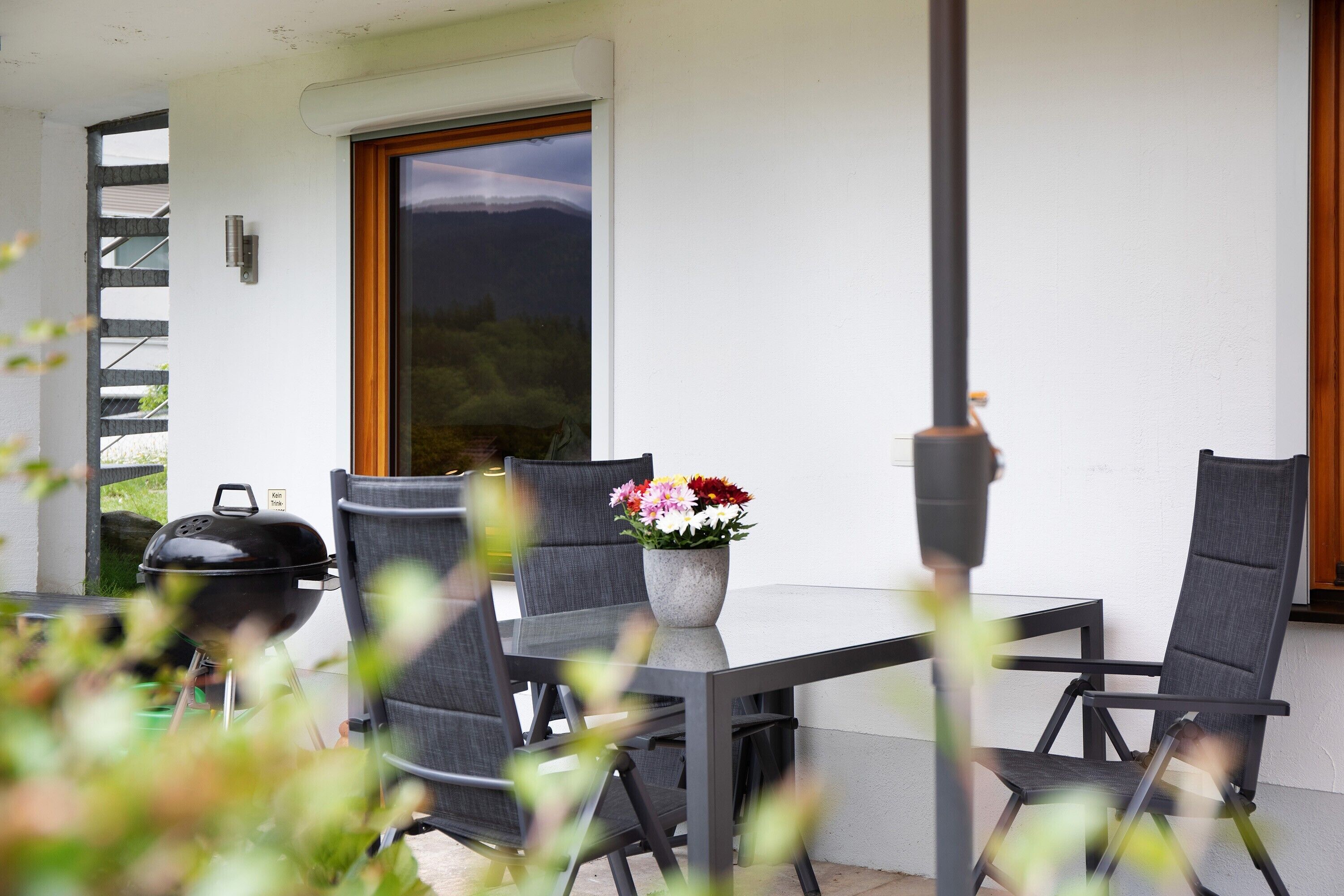 An outdoor patio with a table, chairs, a grill, and a potted plant.