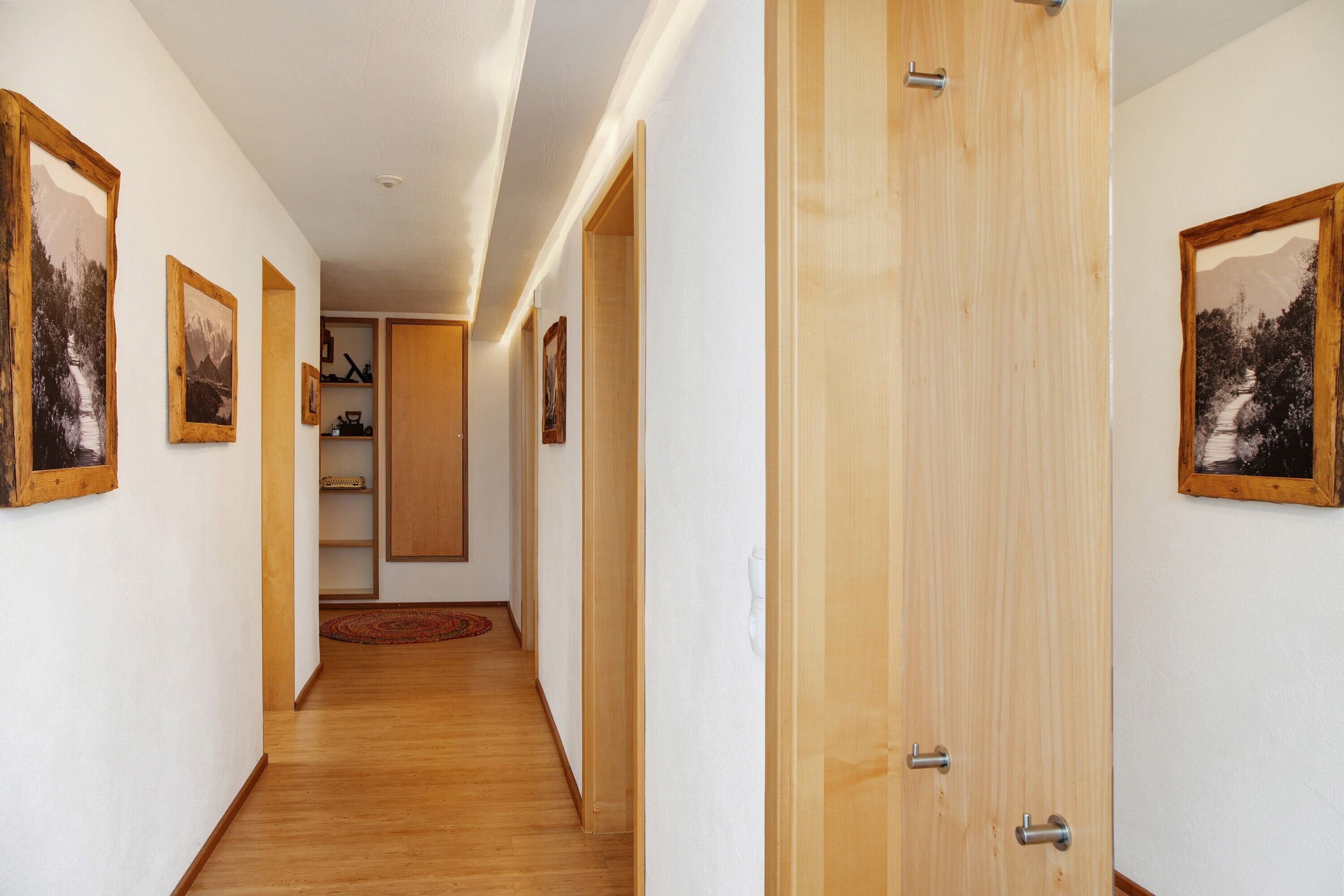 Ein Korridor mit Holzboden, weißen Wänden und gerahmten Bildern.