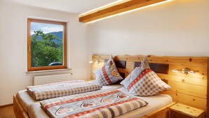 Un dormitorio con cabecera de madera, dos camas con ropa de cama a cuadros, una ventana con vistas a zonas verdes y un radiador.