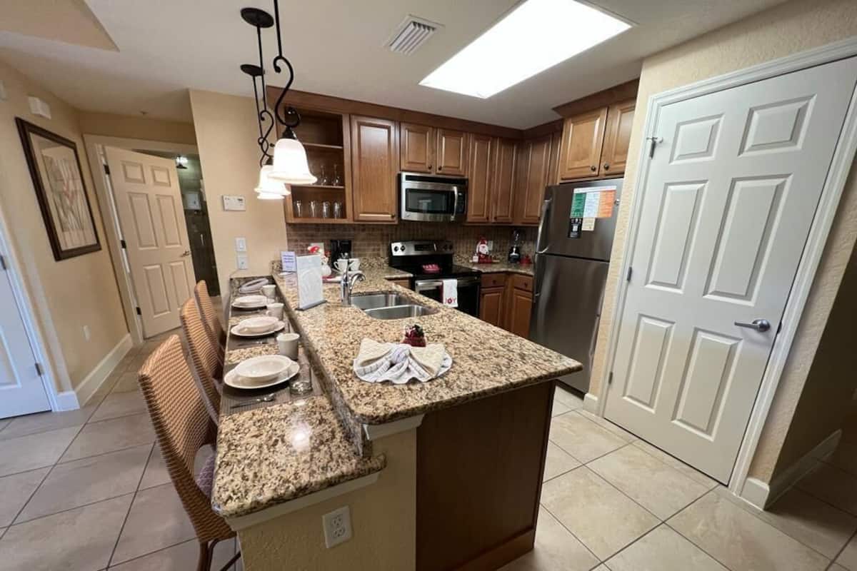 A kitchen with wooden cabinets, a granite countertop, a stainless steel refrigerator, and a microwave.