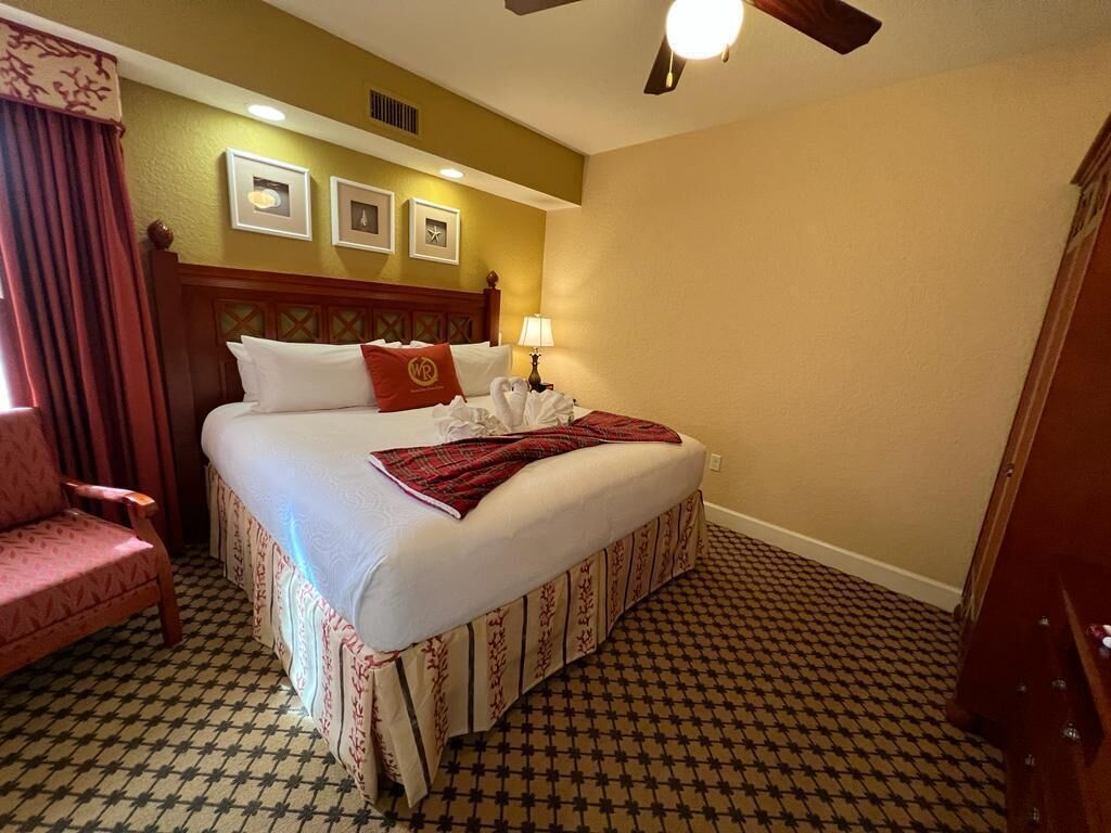 Una habitación de hotel con una cama, una silla, una lámpara y un ventilador de techo.