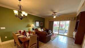 A dining area with a table set for four, a brown leather sofa, a ceiling fan, and a view of a balcony with plants. - Westgate Town Centre Resort (Kissimmee)