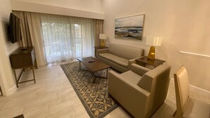 A living room with a sofa, coffee table, and a TV on a stand. There is a painting on the wall and a window with curtains. - Westgate Town Centre Resort (Kissimmee)