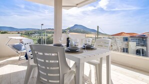 A balcony with a table set for two, overlooking a scenic landscape with hills and a mountain.