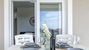 A dining table set with plates, bowls, wine glasses, and a bottle, with a view of the sky and a clock on the wall.