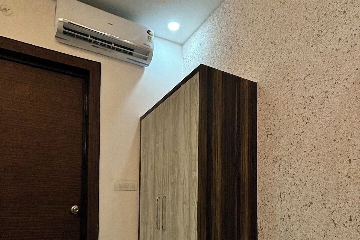 A room with a marble floor, a wardrobe with a wooden finish, a door, and an air conditioning unit on the wall.