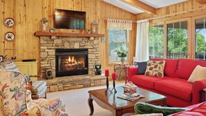 A cozy living room with a stone fireplace, wooden walls, a red sofa, and a ceiling fan.