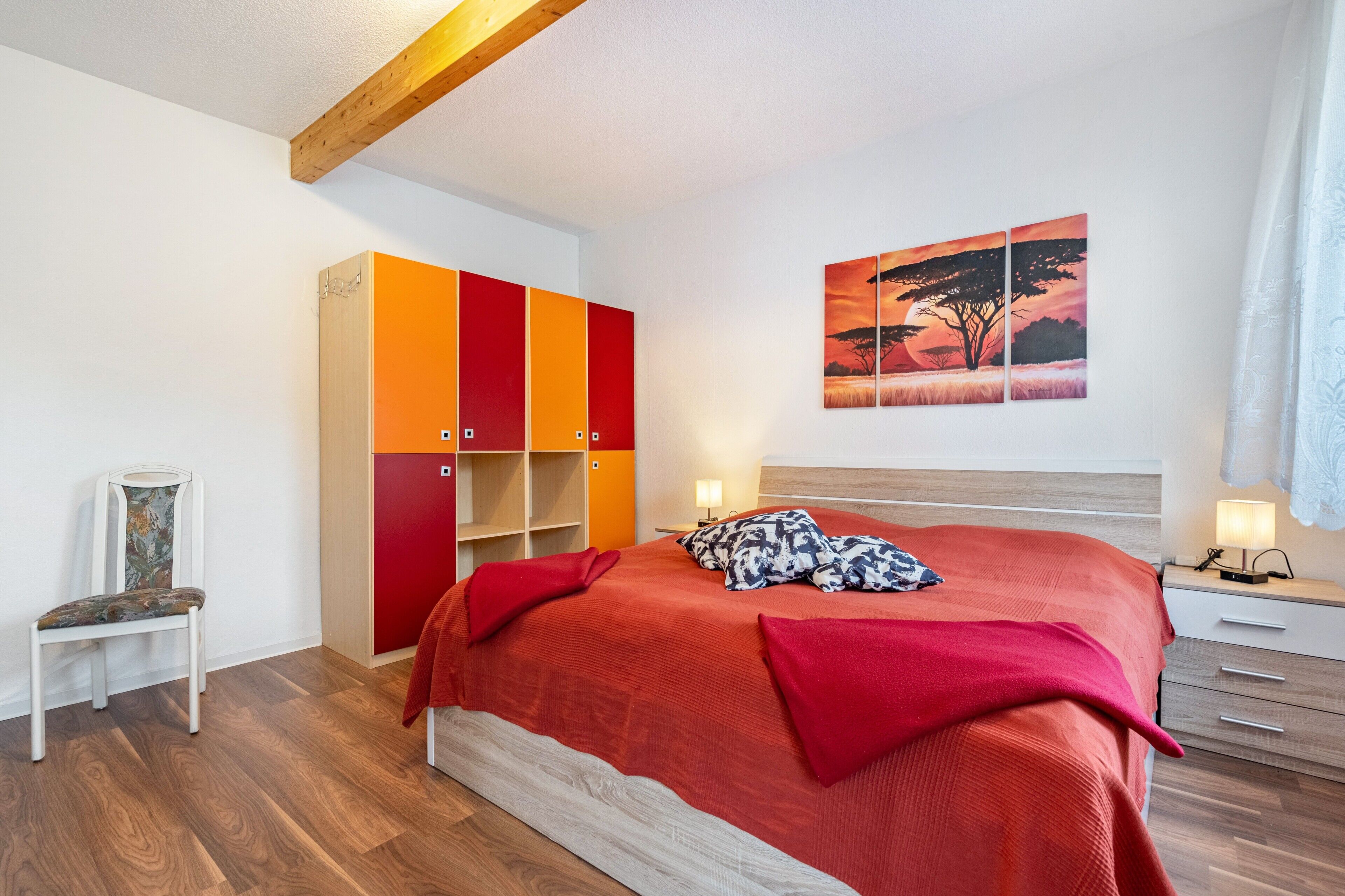 Ein Schlafzimmer mit Bett, Kleiderschrank, Stuhl und einem Bild an der Wand.