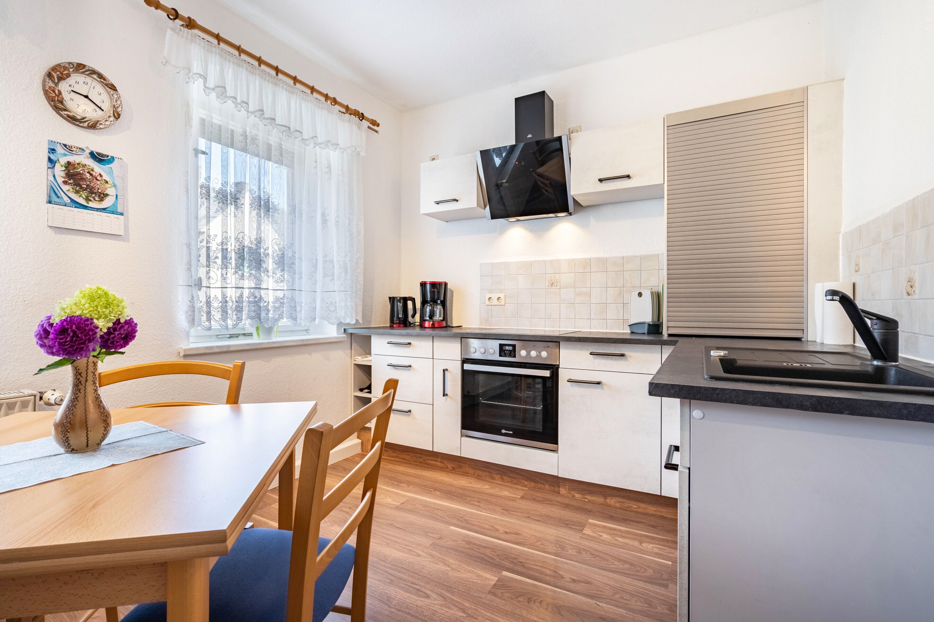 A modern kitchen with a dining area, a built-in oven, a coffee maker, and a TV mounted above the oven.