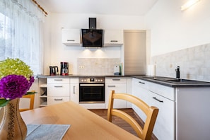 Una cocina moderna con muebles blancos, horno empotrado, cafetera y una mesa de comedor con sillas.