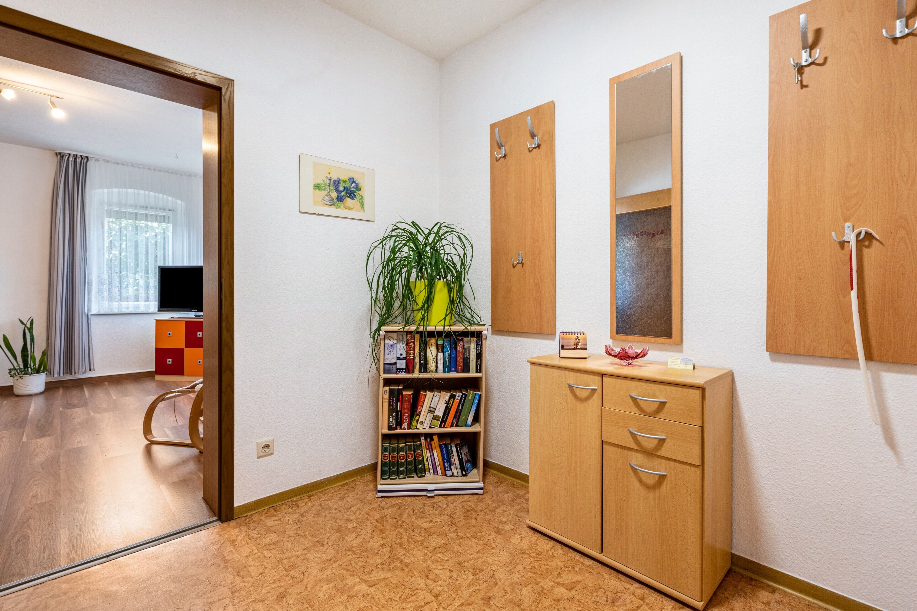 Une chambre d’hôtel avec un plancher en bois, une bibliothèque, une armoire, un miroir et un téléviseur.
