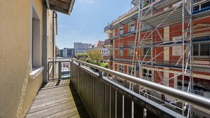 Un balcone con pavimento in legno e ringhiera metallica, con vista su un edificio in costruzione e ponteggi.