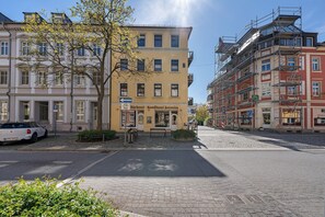 Une rue bordée d’immeubles, avec une voiture garée et un arbre.