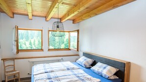 A bedroom with a bed, a chair, a radiator, and three windows with a view of trees.