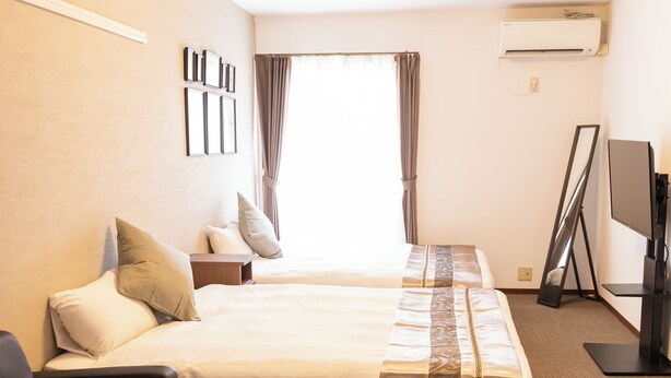 A hotel room with two beds, a sofa, a TV, and a flat-screen TV stand.