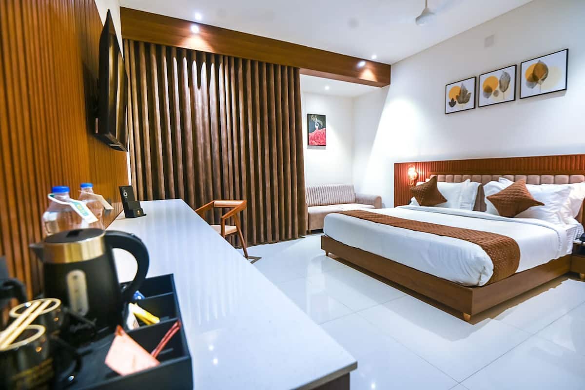 A modern hotel room with a large bed, a desk with a kettle, and a seating area.