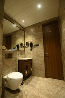 Un baño con inodoro, lavabo, espejo y secador de pelo fijado en la pared.