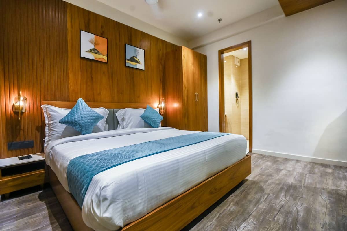 A modern bedroom with a wooden headboard, a large bed with white bedding and blue accents, a nightstand with a phone, and two wall-mounted light fixtures.
