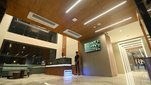 A hotel reception area with a marble floor, wooden ceiling, and a large digital screen displaying a green pattern.