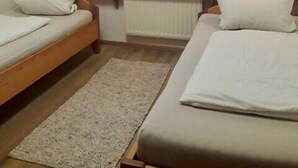 Ein Schlafzimmer mit zwei Betten, einem Fenster mit Vorhängen, einem Heizkörper und einem kleinen Teppich.