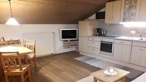 Eine kleine Küche mit Holzausstattung, einem Esstisch und einem Fernseher.