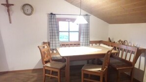 Ein Esszimmer mit Holztisch und -stühlen, einem Kruzifix an der Wand und einem Fenster mit Vorhängen.