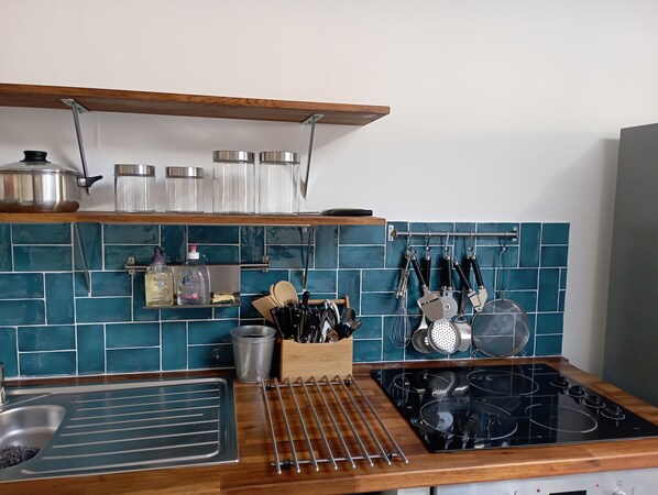 A kitchen with a wooden countertop, stainless steel sink, and a black stove. There are shelves above the counter holding jars and kitchen utensils. - Duplex La Terrasse Jasmin, 3 Chambres, au Coeur du Centre Historique de Mèze ! (Mèze)