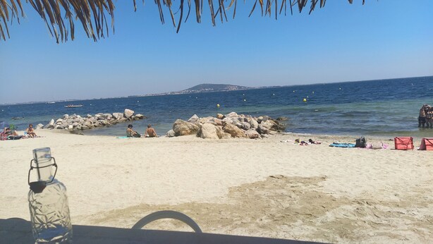 A beach scene with a clear view of the sea, rocks, and distant land.