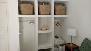 A room with a white wardrobe containing woven baskets, a hat, and a hanging garment.