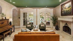 Een ruime woonkamer met een groen plafond, een open haard, een piano en uitzicht op een buitenzwembad door glazen deuren.