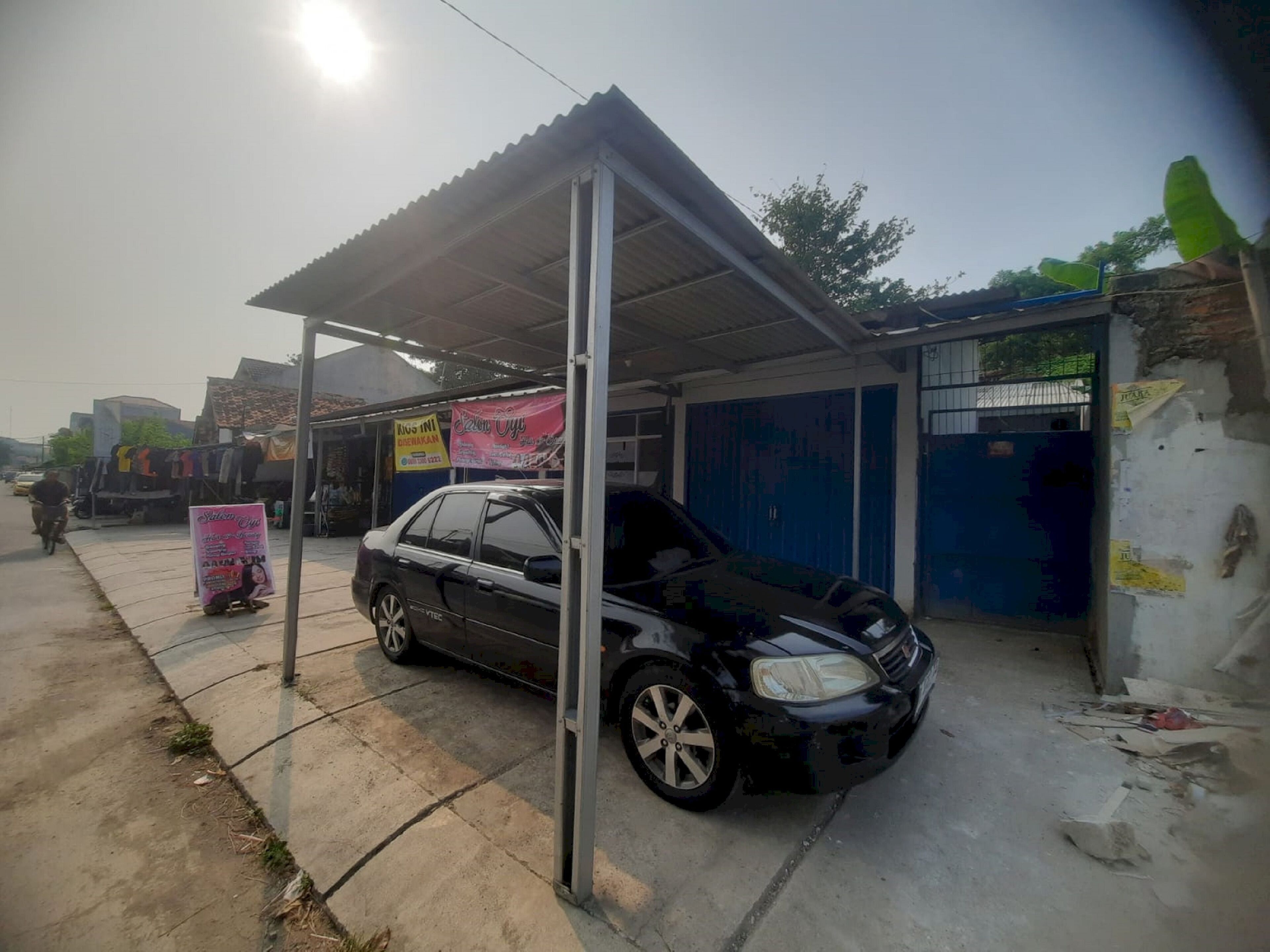 Une voiture est garée sous un auvent métallique dans un parking extérieur dont le sol est en béton.