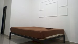 Habitación minimalista con una cama individual, paredes blancas e iluminación empotrada en el techo.