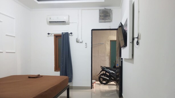 Un dormitorio con una cama, aire acondicionado, una motocicleta y un televisor instalado en la pared.
