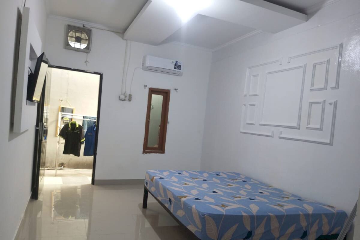 Una habitación pequeña y limpia con una cama, una puerta y un equipo de aire acondicionado en la pared.