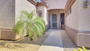 A pathway leading to a building with a cross on the wall, a door with a metal gate, and a palm tree in the foreground. - Surprise Home w/ Pool & Hot Tub! (Surprise)