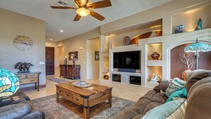 A spacious living room with a ceiling fan, a fireplace, a television, and a large couch. - Surprise Home w/ Pool & Hot Tub! (Surprise)