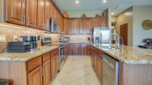 A kitchen with wooden cabinets, granite countertops, stainless steel appliances, and a tiled floor. - Surprise Home w/ Pool & Hot Tub! (Surprise)