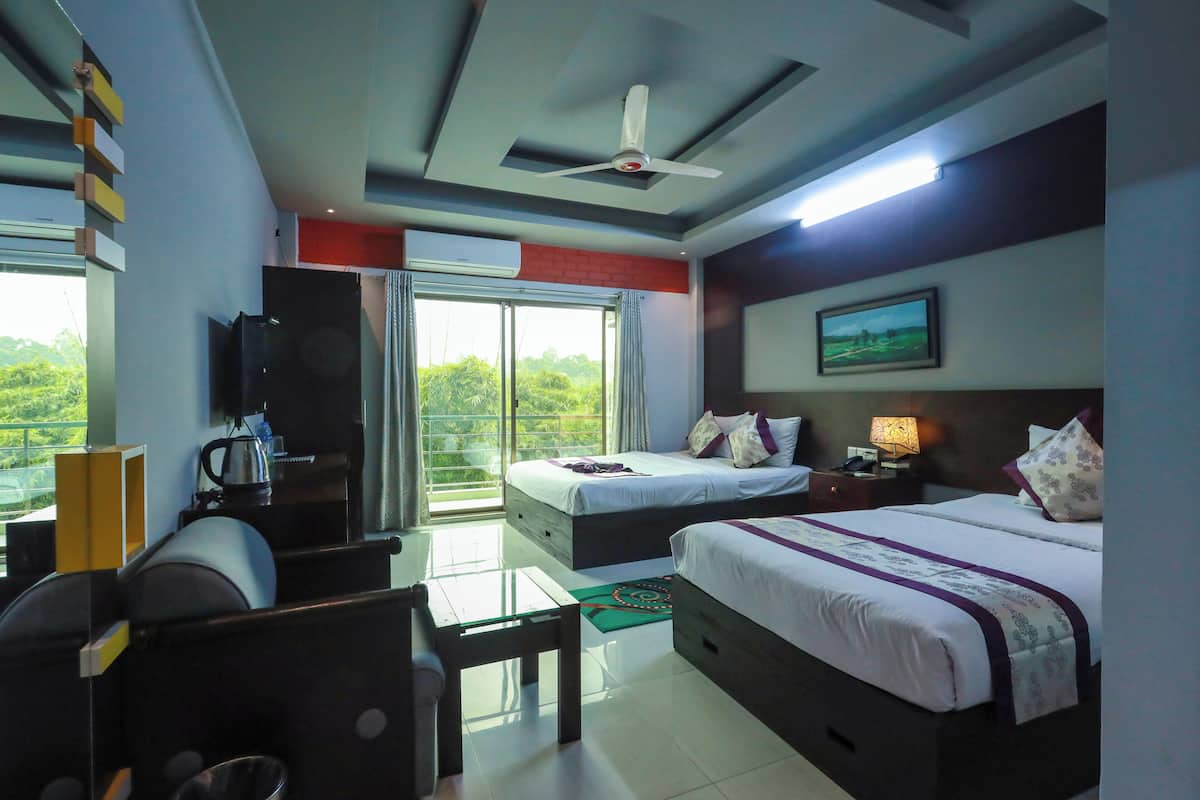 A hotel room with a bed, a desk, a chair, a television, and a balcony with a view of greenery.
