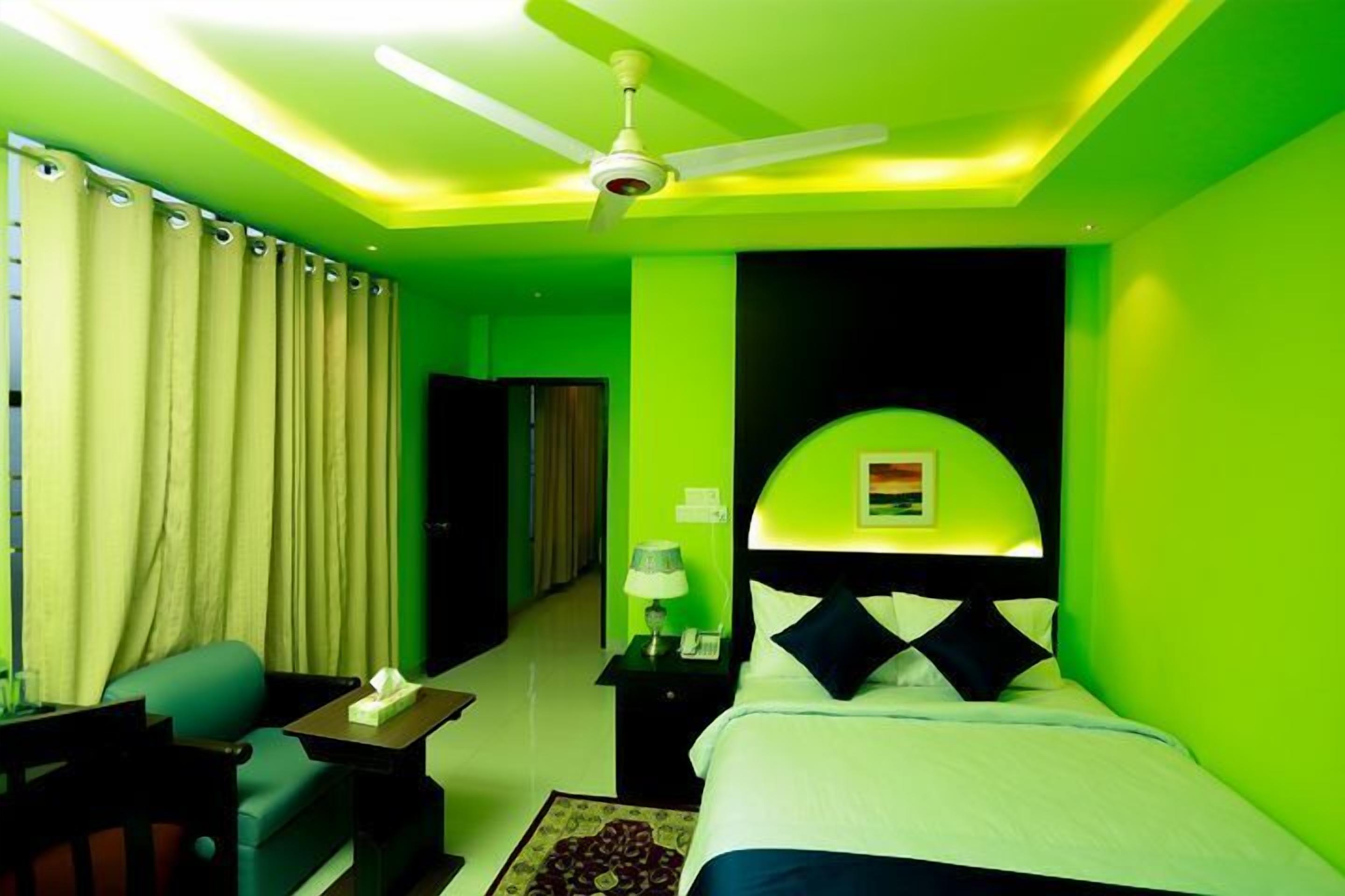 A hotel room with a bed, a desk, a chair, a nightstand, a lamp, a ceiling fan, and a window with curtains.