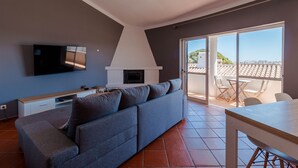Una sala de estar moderna con un sofá gris, un televisor de pantalla plana, una chimenea y un balcón con mesa y sillas.
