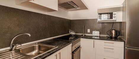 A modern kitchen with a stainless steel sink, a microwave, a kettle, and a refrigerator.