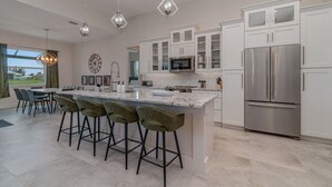 Una cocina moderna con una isla grande, electrodomésticos de acero inoxidable e iluminación colgante.